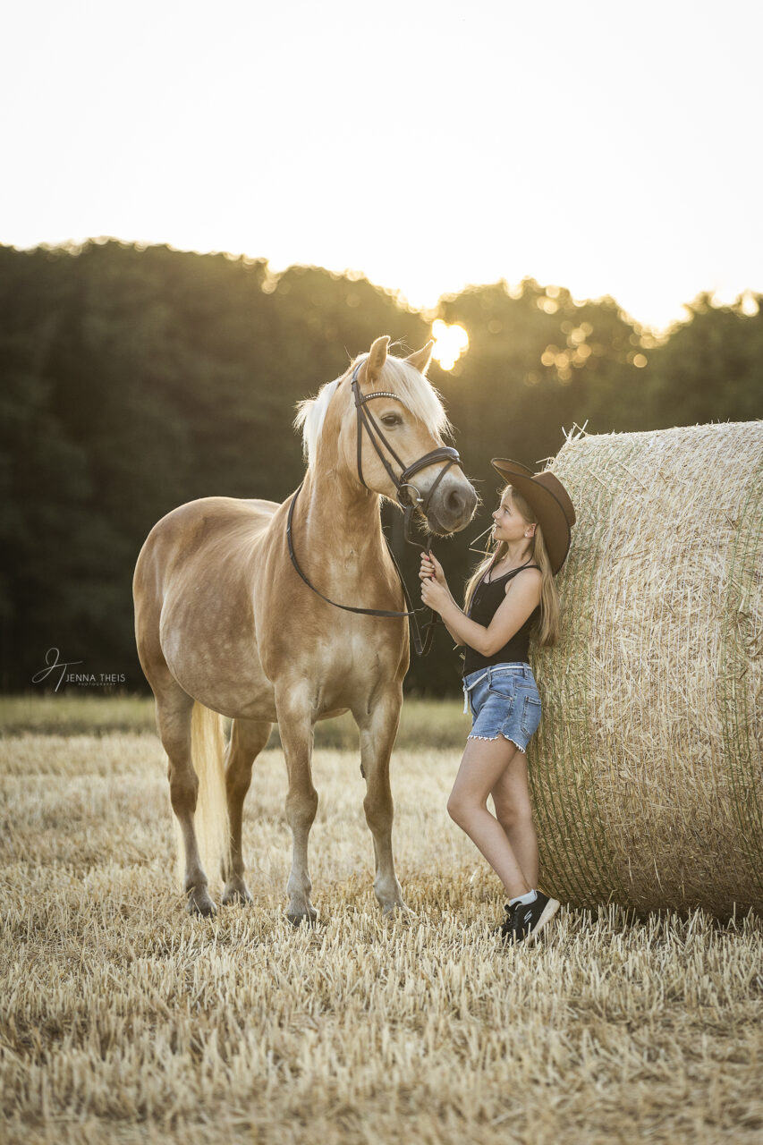 Junges Mädchen mit Westernhut mit ihrem Haflinger auf einem Stoppelfeld mit Strohballen