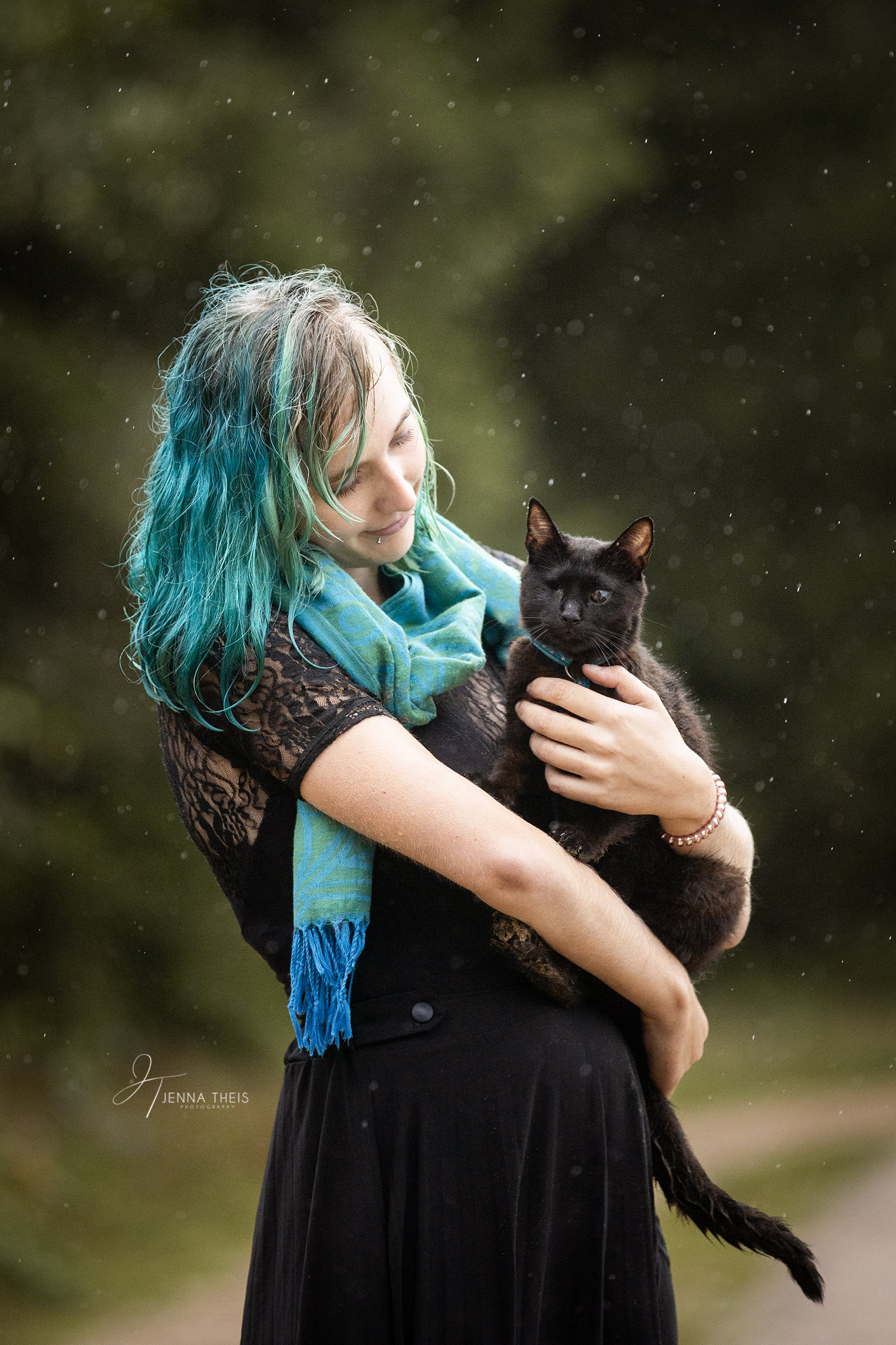 Frau mit blauen Haaren steht im Regen und hält ihre einäugige schwarze Katze auf dem Arm