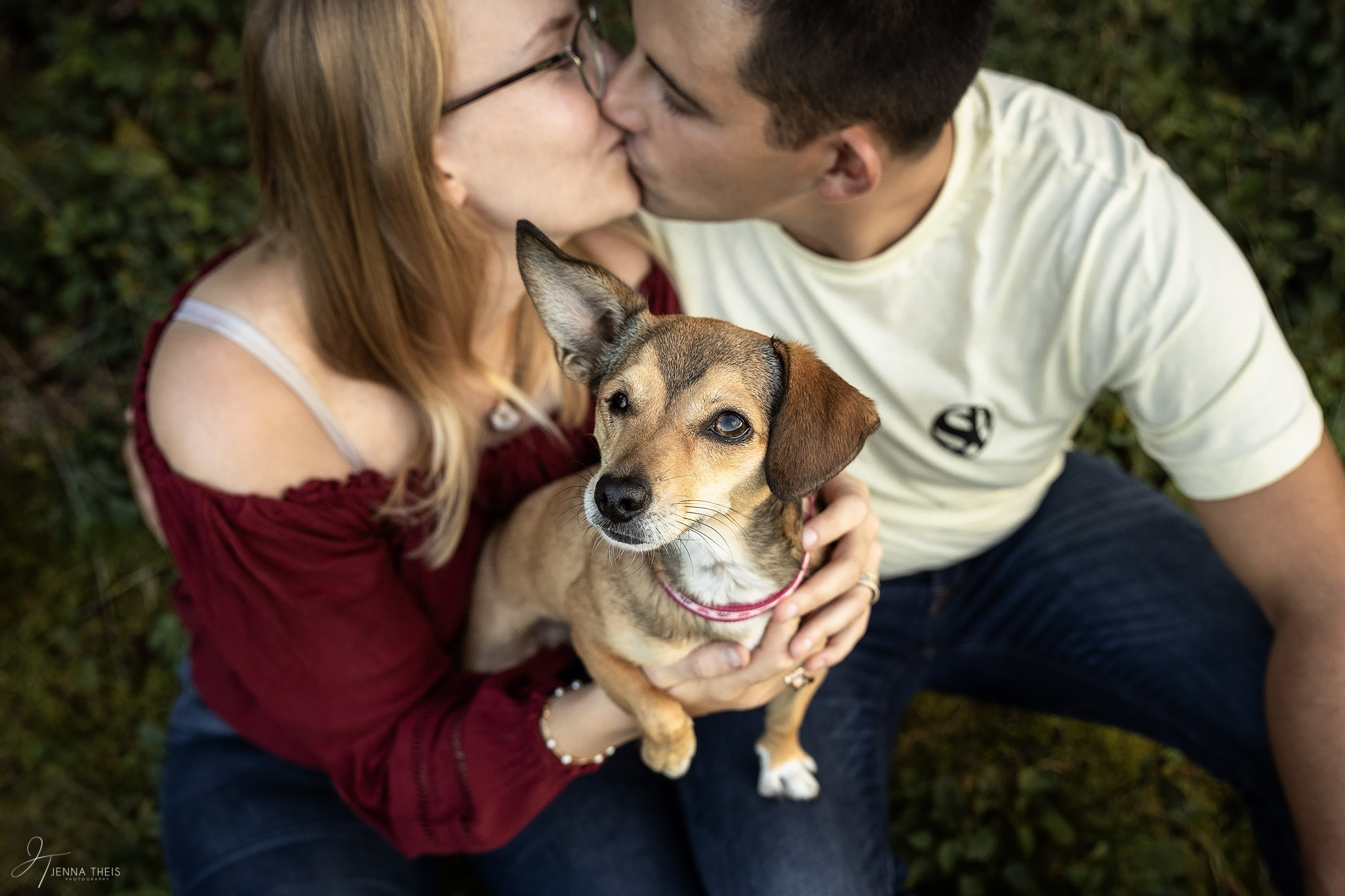 Blinder Hund sitzt auf dem Schoß seiner Besitzerin und schaut in die Kamera, Pärchen sitzt auf dem Boden und küsst sich