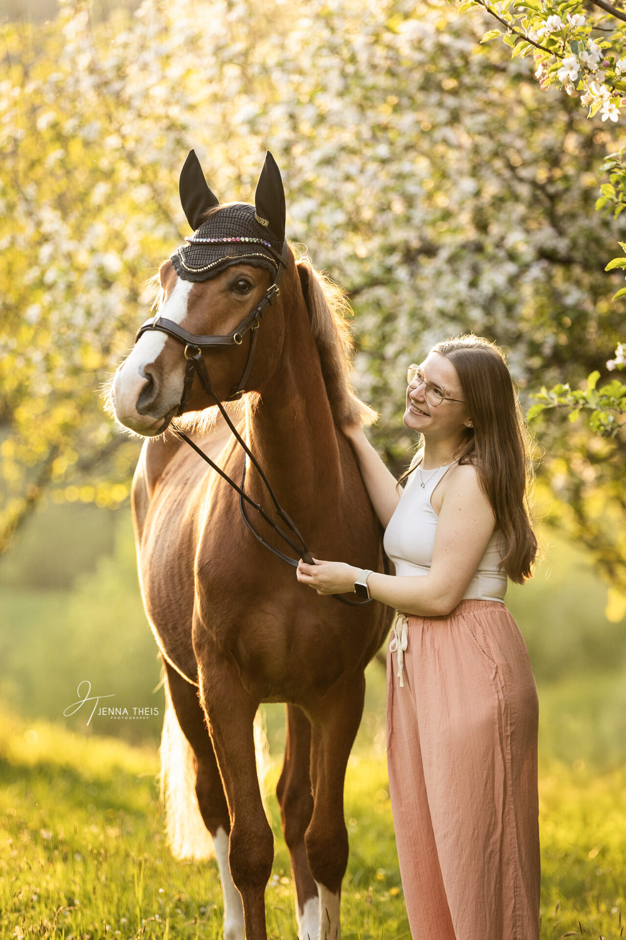 Junge Frau steht mit ihrem deutschen Reitpony vor blühenden Apfelbäumen