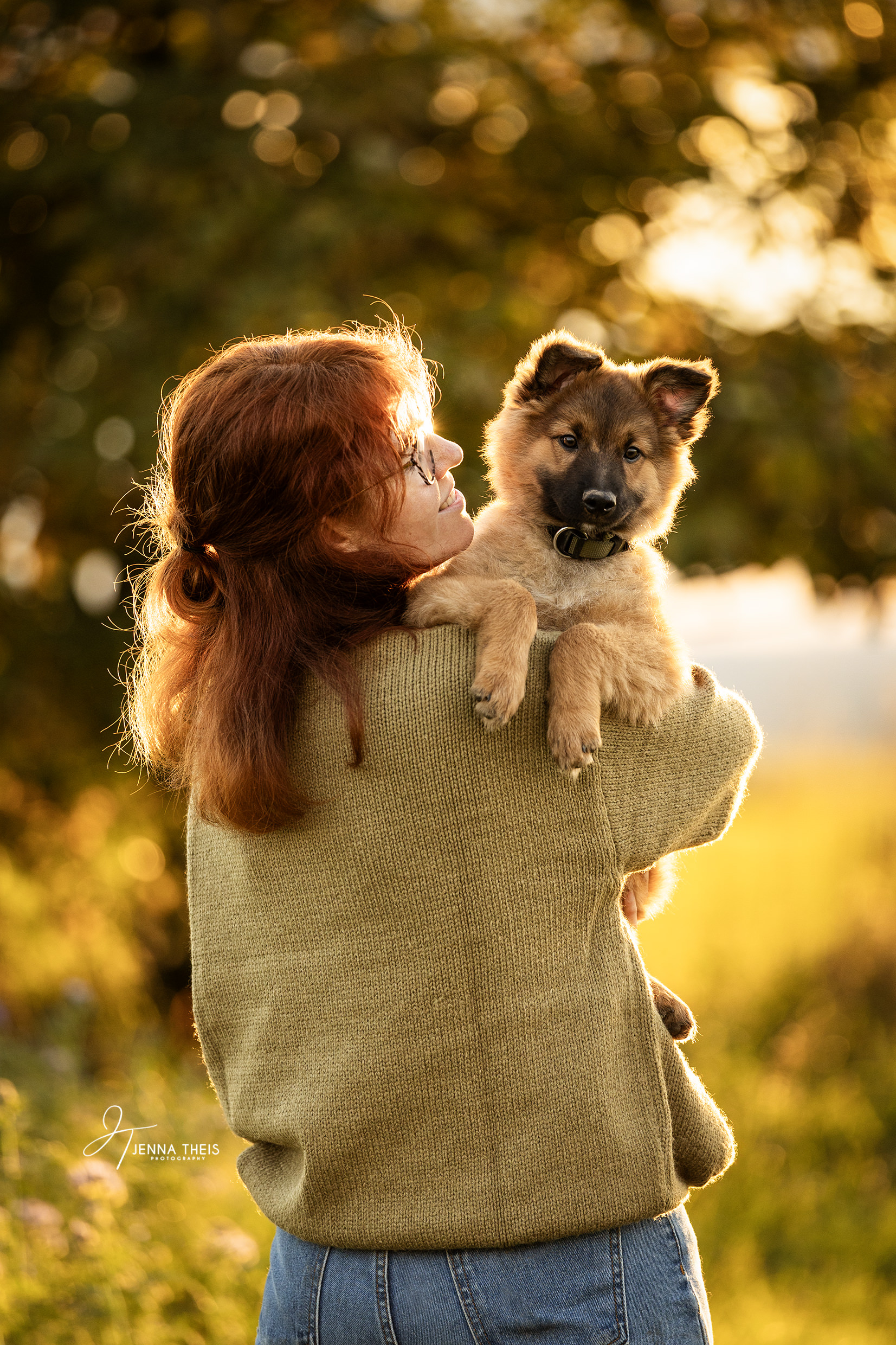 Welpe auf dem Arm seiner Besitzerin im Sonnenuntergang